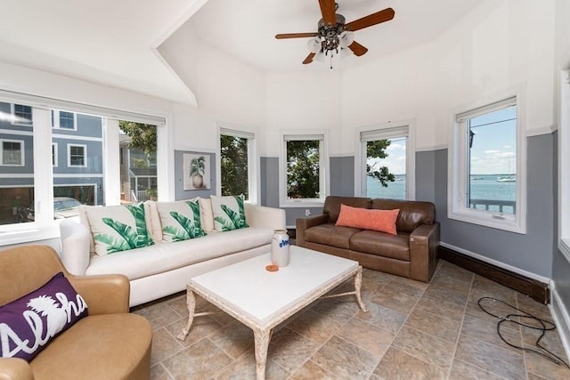 living room with plenty of natural light, ceiling fan, a towering ceiling, baseboards, and stone finish floors