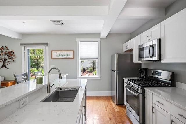 599 Washington St Unit 1, Pembroke, MA 02359 - kitchen featuring appliances with stainless steel finishes, light stone counters, beamed ceiling, white cabinetry, and light wood-type flooring