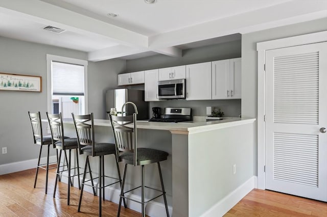 599 Washington St Unit 1, Pembroke, MA 02359 - kitchen with appliances with stainless steel finishes, a kitchen breakfast bar, white cabinetry, light countertops, and beam ceiling