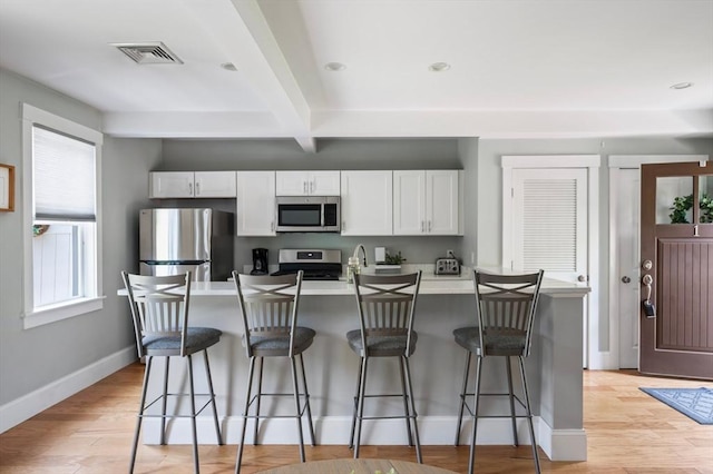 599 Washington St Unit 1, Pembroke, MA 02359 - kitchen featuring appliances with stainless steel finishes, beamed ceiling, white cabinets, a kitchen breakfast bar, and light wood-type flooring
