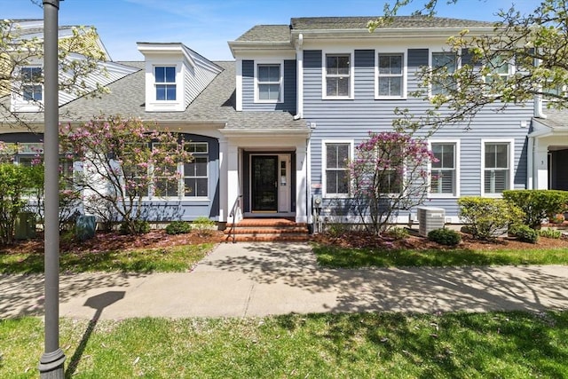 colonial inspired home with a shingled roof and central AC unit