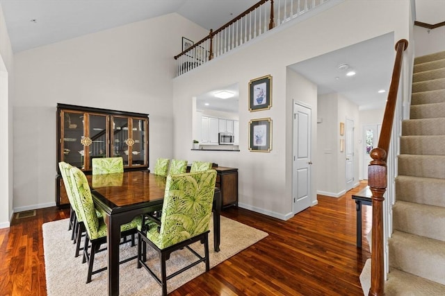 dining space featuring stairs, baseboards, wood finished floors, and a towering ceiling