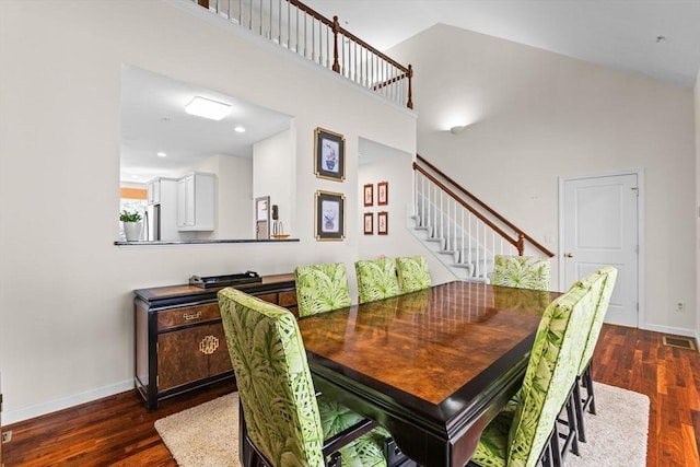 dining room featuring stairs, baseboards, a towering ceiling, visible vents, and dark wood-type flooring