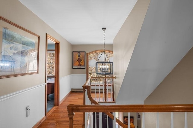 hall featuring light wood-style flooring, a wainscoted wall, a chandelier, and an upstairs landing
