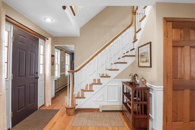 entrance foyer featuring light wood-type flooring, wainscoting, a baseboard heating unit, and stairway