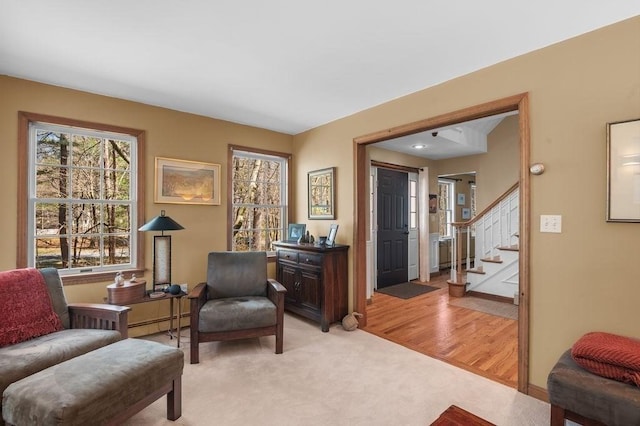 living area featuring stairs, a baseboard heating unit, and light colored carpet