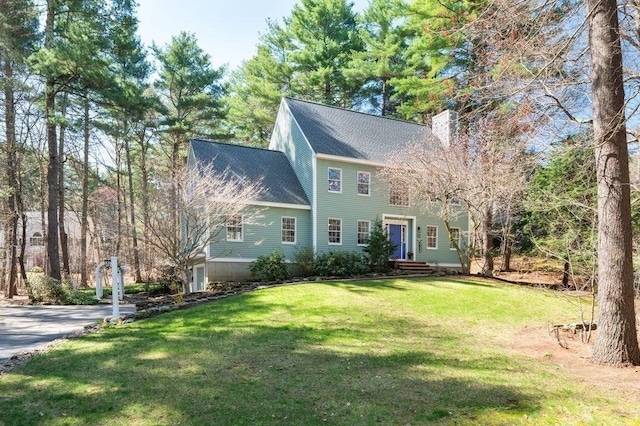 view of front facade featuring a shingled roof, a chimney, and a front lawn