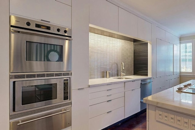 kitchen featuring sink, backsplash, stainless steel appliances, ornamental molding, and white cabinets