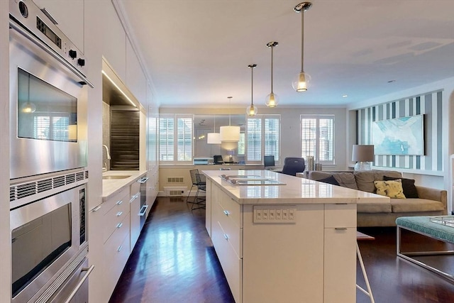 kitchen with pendant lighting, a wealth of natural light, white cabinetry, stainless steel appliances, and a center island with sink