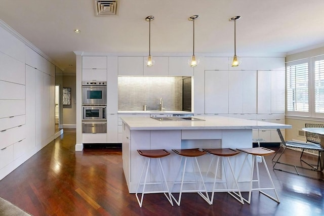 kitchen with pendant lighting, crown molding, a kitchen breakfast bar, black electric stovetop, and white cabinets