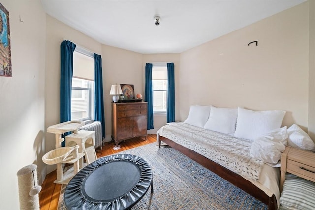 bedroom with multiple windows, hardwood / wood-style flooring, and radiator heating unit