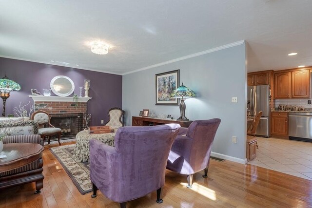 living room with light wood-style flooring, a brick fireplace, crown molding, and recessed lighting