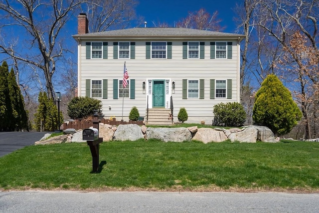 colonial house featuring a front yard, entry steps, and a chimney