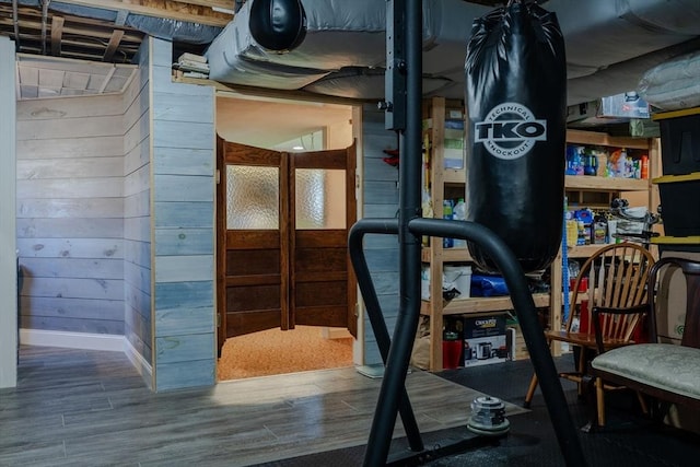 exercise room with baseboards, wooden walls, and wood finished floors