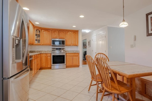 kitchen with light stone counters, stainless steel appliances, light tile patterned floors, glass insert cabinets, and tasteful backsplash