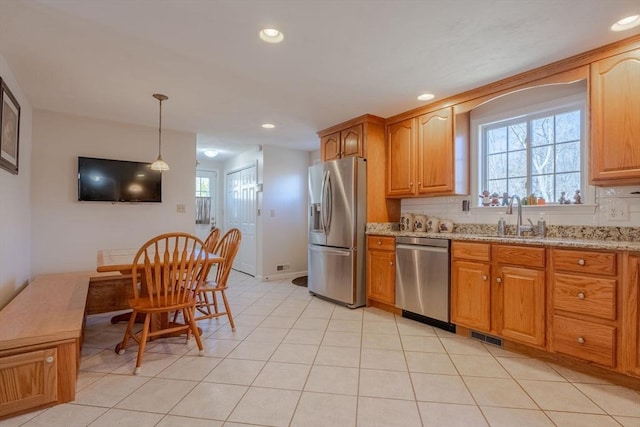 kitchen featuring stainless steel appliances, a sink, recessed lighting, light stone countertops, and decorative light fixtures