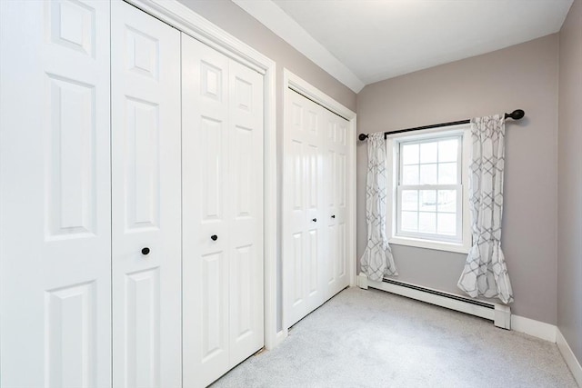 unfurnished bedroom featuring two closets, a baseboard radiator, and light colored carpet