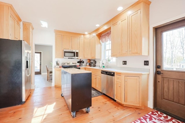 kitchen with sink, stainless steel appliances, a kitchen island, light wood-type flooring, and light brown cabinets