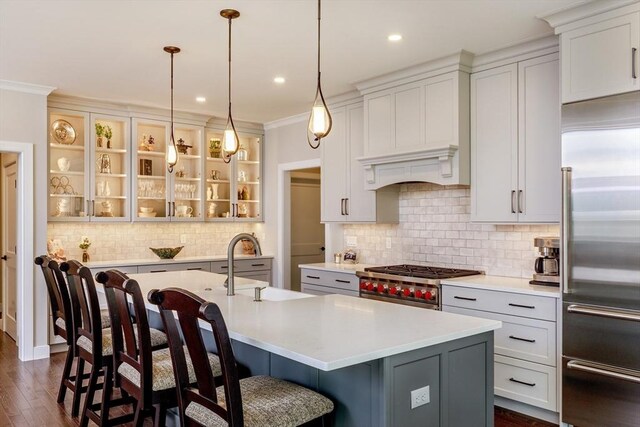kitchen with an island with sink, a kitchen bar, light countertops, stainless steel built in fridge, and backsplash