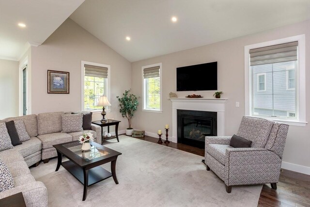 living area with a glass covered fireplace, baseboards, recessed lighting, light wood-type flooring, and vaulted ceiling