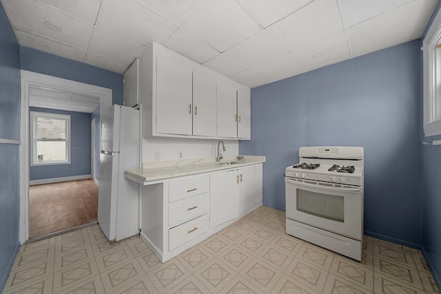 kitchen featuring light countertops, a sink, white cabinetry, white appliances, and a drop ceiling