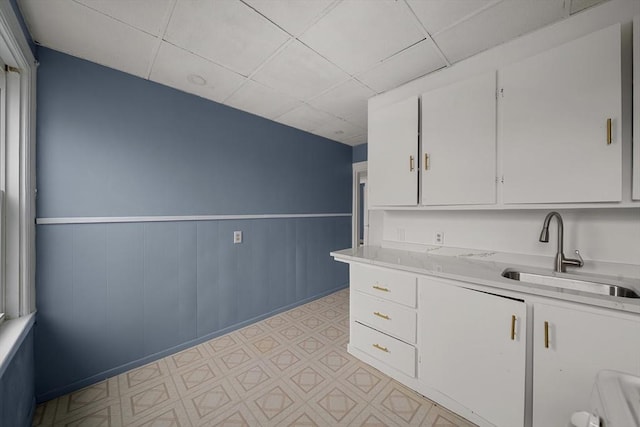 kitchen featuring white cabinetry, a drop ceiling, a wainscoted wall, a sink, and light floors