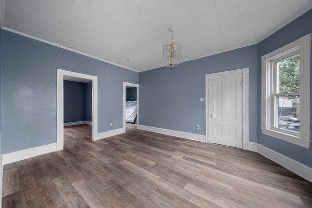 spare room featuring crown molding, baseboards, wood finished floors, and a notable chandelier
