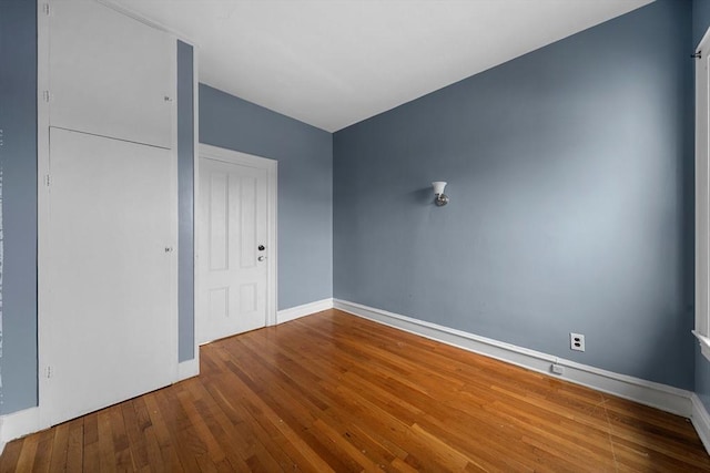 unfurnished bedroom featuring wood-type flooring, a closet, and baseboards