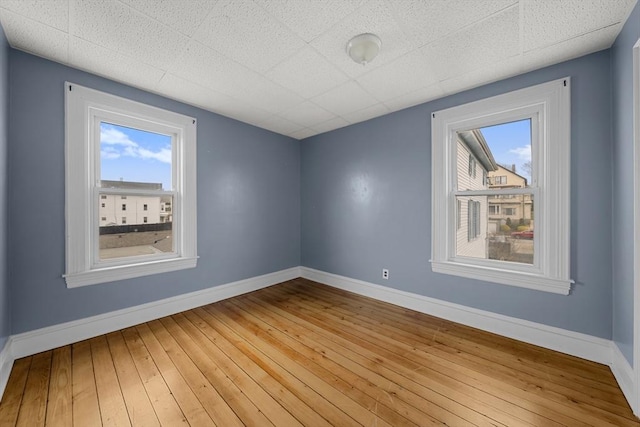 spare room with baseboards, a paneled ceiling, and hardwood / wood-style flooring
