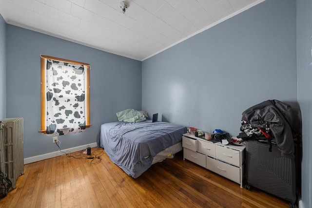 bedroom featuring wood-type flooring, radiator, baseboards, and ornamental molding