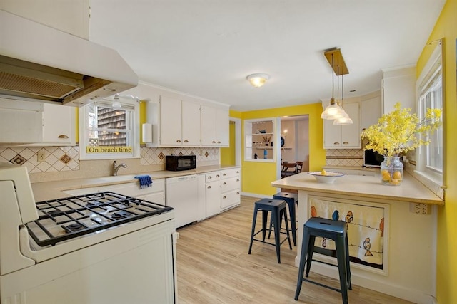 kitchen featuring white appliances, white cabinets, light countertops, a kitchen bar, and decorative light fixtures