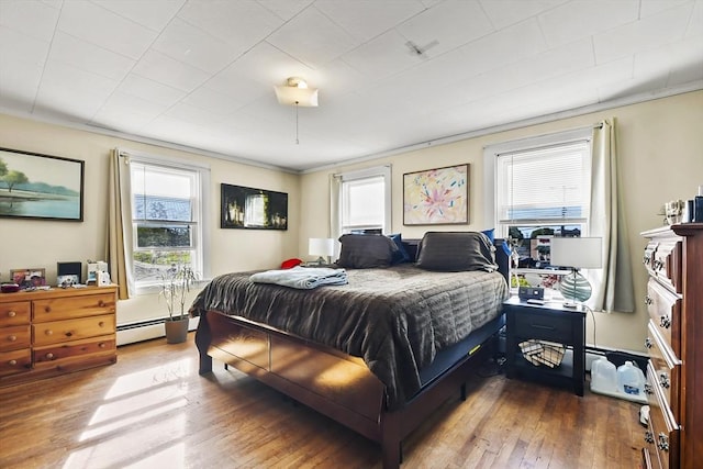 bedroom featuring multiple windows, a baseboard heating unit, hardwood / wood-style floors, and ornamental molding