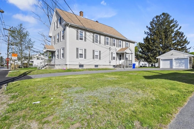 view of side of home featuring a chimney, a detached garage, a yard, and an outbuilding
