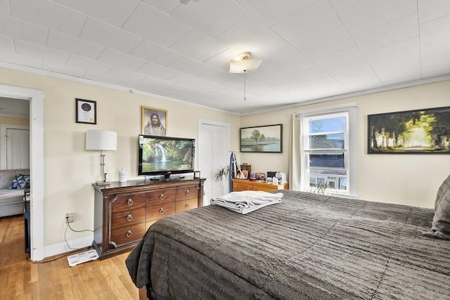 bedroom featuring light wood finished floors, baseboards, and ornamental molding