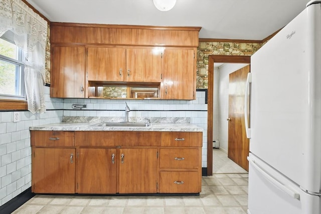 kitchen featuring freestanding refrigerator, a sink, light countertops, brown cabinetry, and tile walls