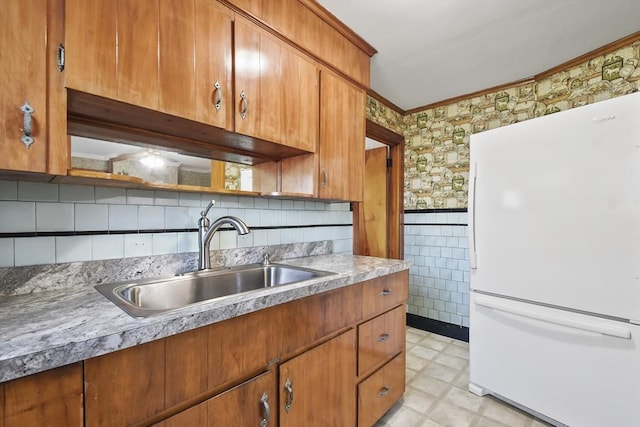 kitchen with freestanding refrigerator, a sink, tile walls, brown cabinets, and ornamental molding