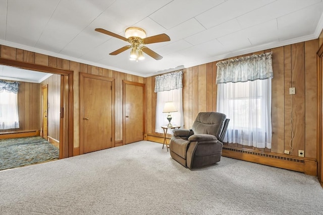 sitting room with a baseboard heating unit, plenty of natural light, ornamental molding, wood walls, and ceiling fan
