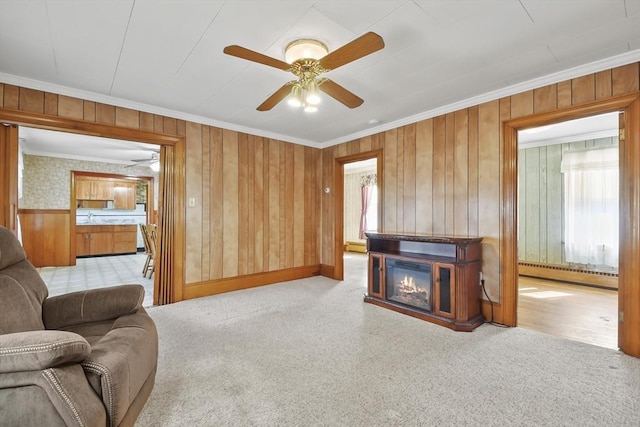 living room featuring baseboard heating, ornamental molding, healthy amount of natural light, wood walls, and ceiling fan