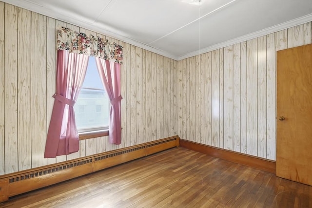 spare room with baseboard heating, wood finished floors, and wooden walls