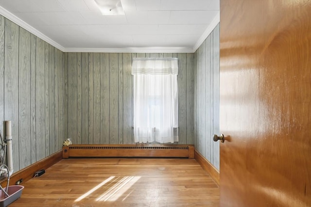 empty room featuring wood finished floors, a baseboard heating unit, baseboards, and ornamental molding