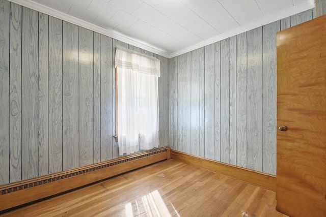 empty room with baseboard heating, wood finished floors, wood walls, baseboards, and crown molding