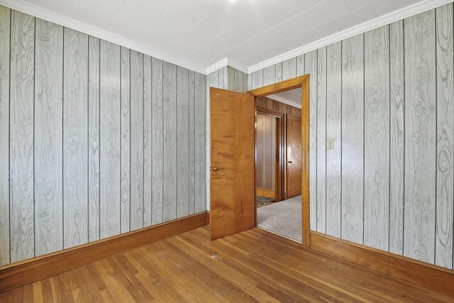 unfurnished room featuring crown molding, wood finished floors, wooden walls, and baseboards