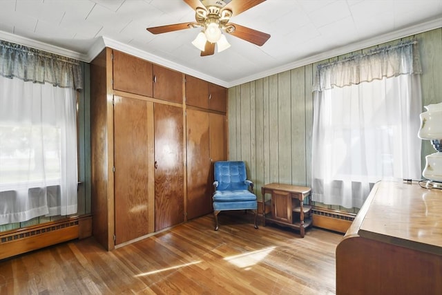 living area with crown molding, a baseboard radiator, light wood-style floors, a ceiling fan, and a baseboard heating unit