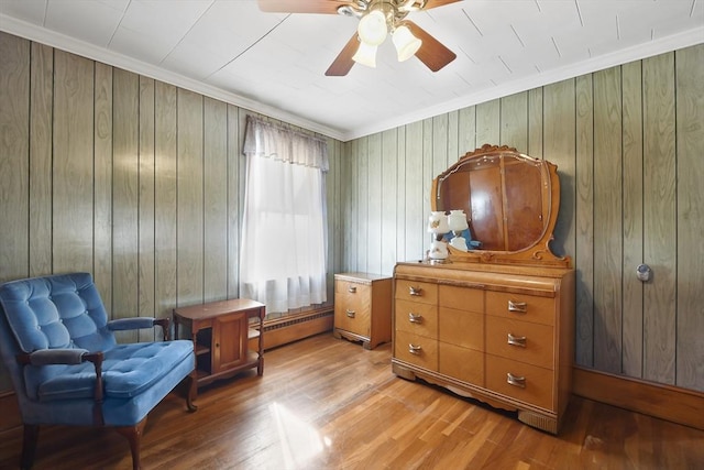 living area with baseboard heating, light wood-type flooring, wood walls, a ceiling fan, and crown molding