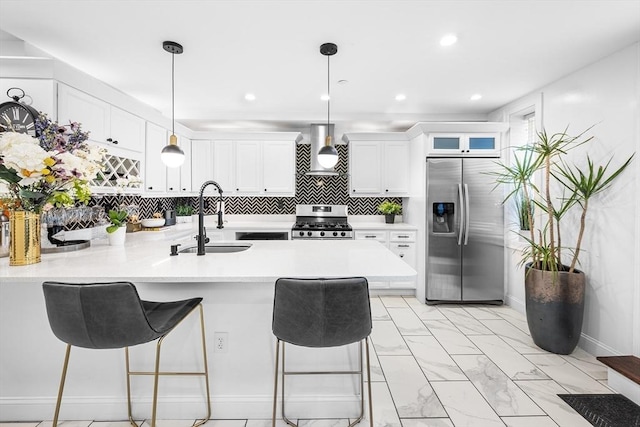 kitchen with appliances with stainless steel finishes, a sink, wall chimney exhaust hood, a peninsula, and light marble finish flooring