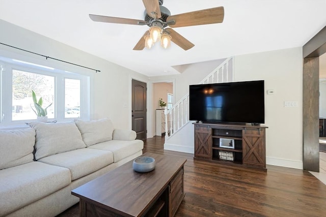 living room featuring dark wood-style floors, a ceiling fan, baseboards, and stairs