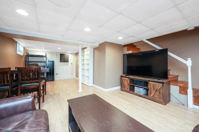 living area featuring light wood-type flooring, a paneled ceiling, baseboards, and stairs