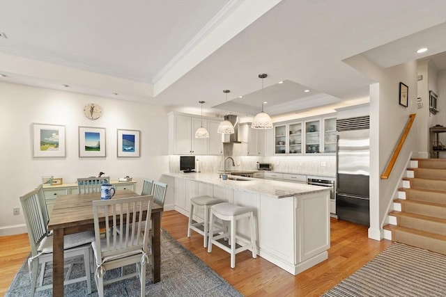 kitchen featuring a tray ceiling, appliances with stainless steel finishes, a peninsula, light wood-style floors, and white cabinets