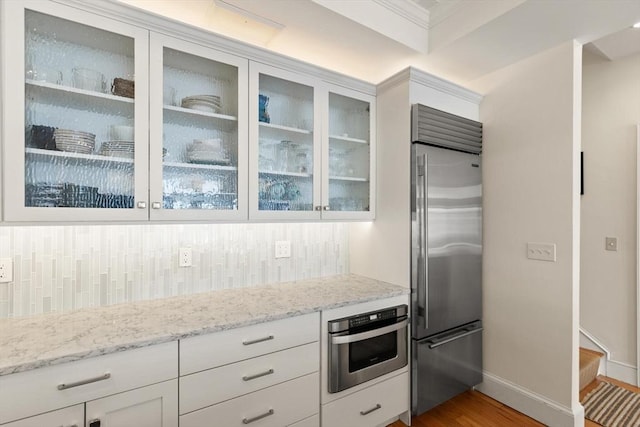 kitchen with light stone counters, backsplash, white cabinetry, appliances with stainless steel finishes, and glass insert cabinets