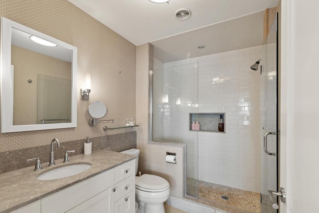 full bathroom featuring wallpapered walls, a shower stall, toilet, and vanity